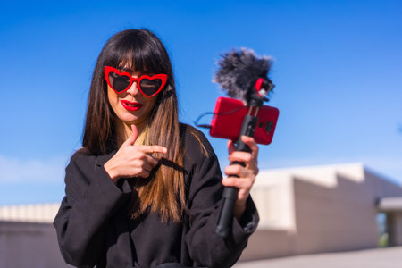 Brunette caucasian girl making a vlog on Valentine's day for social networks, red hearts sunglasses,...