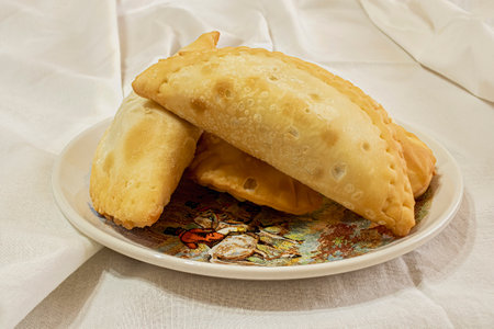 Fried empanadas. Traditional Argentine food on a decorated plate and cloth tablecloth.
