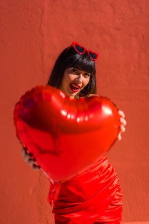 Caucasian brunette girl with heart balloons on Valentine's day wearing sunglasses, red background....