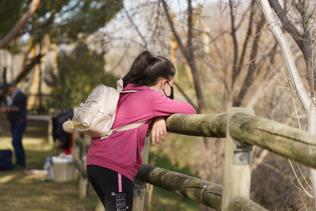 Girl leaning against a wooden fence with a backpack in a park, Madrid, Spainの写真素材