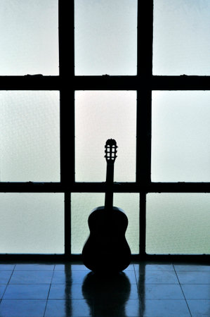 Acoustic guitar silhouette against windowの写真素材