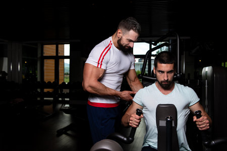 Personal Trainer Showing Young Man How To Train Back On Machine In The Gym