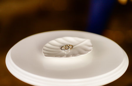 gold wedding rings lie on a white stand in the form of a leaf from a treeの写真素材