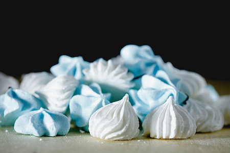 white and blue meringue in the form of drops, lies on a brown table on a black background. Side view.の写真素材