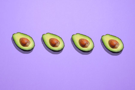 Avocados in a row over purple background.