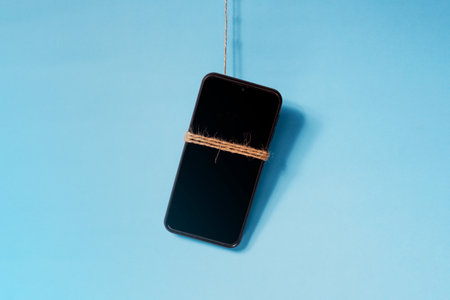 old scrap cell phone hanging by a wire on a light blue background