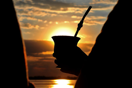 Silhouette of hands holding a yerba mate traditional South American drink in a beautiful sunset viewの写真素材