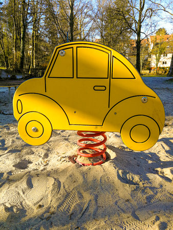 Spring seesaw in the shape of a stylized car on an empty children's playground with a sandy floor