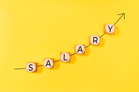 Salary raise concept. Rising arrow and word on wooden blocks on yellow background. Copy space