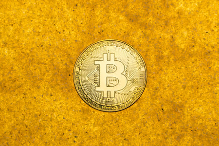 one bitcoin crypto coin on a shiny golden sand background with backlight, top view.
