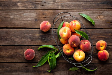 Fresh peaches fruits with leaves in basket on dark wooden rustic background, top viewの写真素材