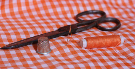 Orange and White Checkered Fabric With Thimble and Spool of Orange Thread. Vintage Scissors in Backgroundの写真素材
