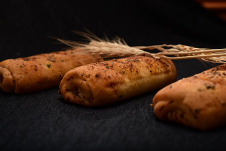 Bread roll and bunch of wheat on black background. food background concept.の写真素材