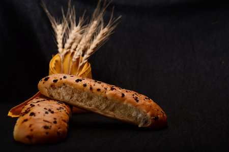 Bread roll and bunch of wheat on black background. food background concept.の写真素材