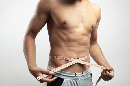 In white background a fit young white guy measuring his waist size with tape measure.の写真素材