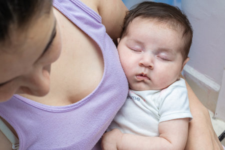beautiful latin baby girl sleeping tenderly in her mother's arms while mom looks away. woman in...