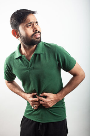 young man feeling strong stomach pain or stomach acidity isolated in white background.の写真素材