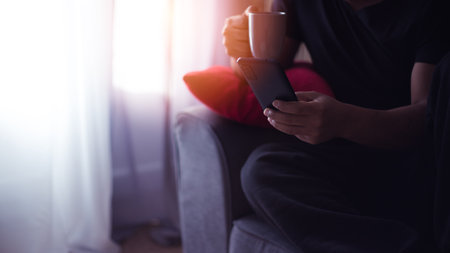 handsome young Hispanic at home drinking coffee and using his smart phoneの写真素材
