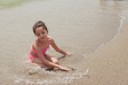 Girl in a pink bikini playing happily on the shore of the beach with the waves on a sunny summer day, Vera, Spainの写真素材