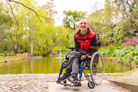 Portrait of a paralyzed young man in a public park in the city. Sitting in the wheelchair