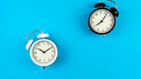 Selective focus on a black and white alarm clock on a blue background. A copy space of a clock...