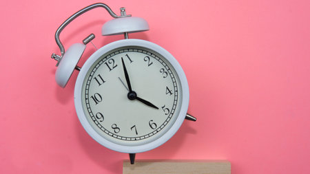 Selective focus on a white alarm clock on a pink background. A fallen white alarm clock showing how time cannot be wasted.の写真素材