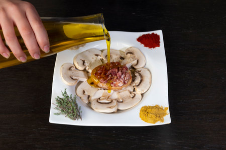 one hand pouring oil on a plate of mushrooms on a wooden board. mediterranean foodの写真素材