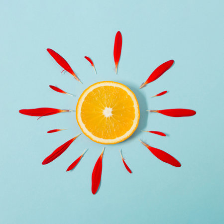 Sun made of orange and red flower petals on bright blue background. Fruit summer minimal concept.の写真素材