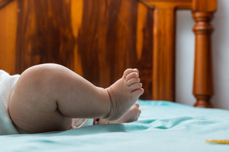 close-up detail of the feet of a latina baby girl lying on a bed with blue sheets. feet of a chubby baby girl, with kicking motion and shrunken toes.の写真素材