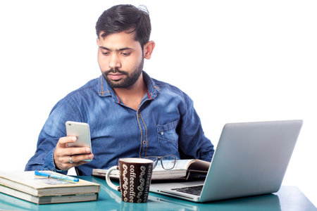 distracted man looking at mobile phone screen while working on laptop