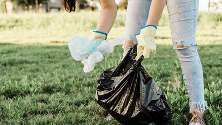 Person caring for our planet earth by collecting garbage from the ecosystem, dressed in jeans, a white shirt and yellow gloves.の写真素材