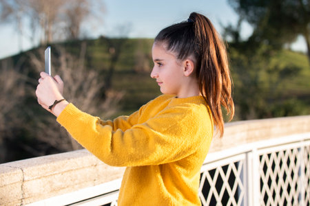 girl in a yellow sweater making a selfie in a park. concept of technology, youth, natureの写真素材