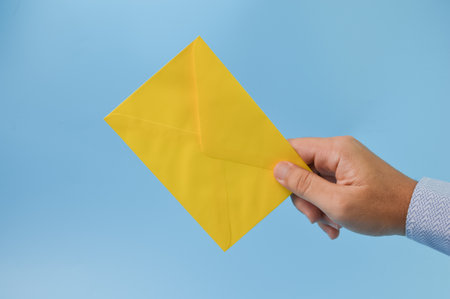 Hand holding yellow envelope isolated on a blue backgroundの写真素材