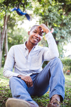 A vertical shot of a smiling African-American male sitting in the parkの写真素材