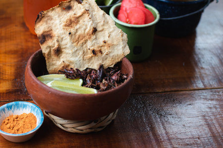 A closeup of a wooden bowl full of dried caramelized bugs with bread on the sideの写真素材