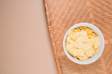 A bowl of cornflakes on a wooden placemat isolated on beige surface  with free space for text