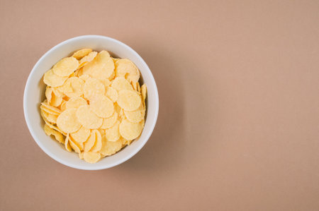 A bowl of cornflakes isolated on a brown background with free space for textの写真素材