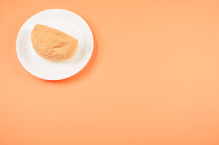 A top view of half bread bun on a plate isolated on light orange background