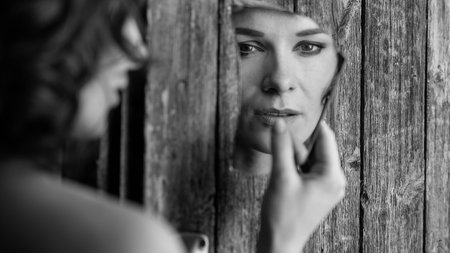 A grayscale portrait of a female holding a broken mirror on the wooden backgroundの写真素材