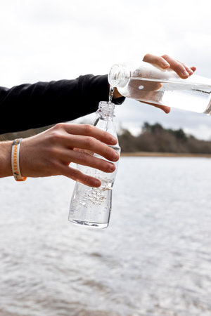 A vertical shot of man's hands filling a water from one bottle to another