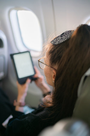 Woman sitting near window and reading ebook during flight on planeの写真素材