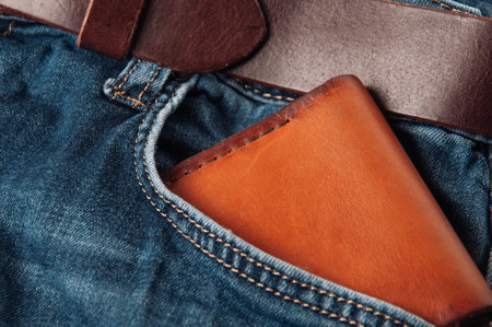 A closeup shot of a brown leather wallet in the jeans pocket with a leather belt