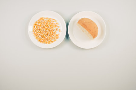 A top view of half bread bun and corn grains on a plate isolated on white backgroundの写真素材