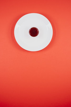 A vertical shot of a bowl of jam on a plate on a red surfaceの写真素材