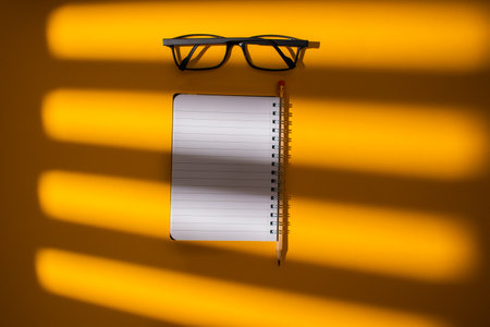 A closeup of a bright orange shadowy surface with a pair of glasses and a notebook on itの写真素材