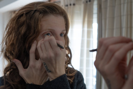 A closeup shot of a Caucasian female applying makeup in front of a mirrorの写真素材