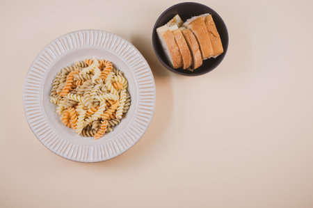 A plate of pasta twists and a bowl of sliced bread on a beige background with free space for text