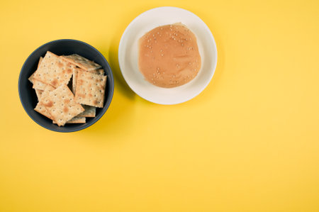 A bowl of square crackers and bread bun on a plate isolated on yellow backgroundの写真素材