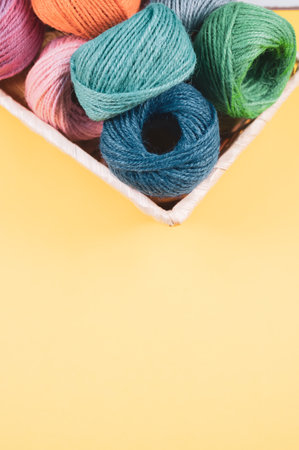 A basket full of colorful yarn rolls isolated on a yellow background with free space for text