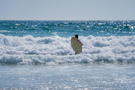 A person holding a surfboard trying to surf in the wavy sea on the coast